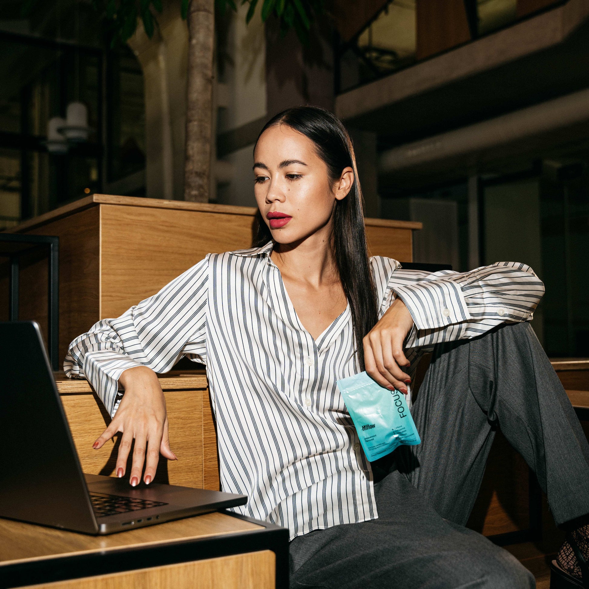 Woman working on a laptop with a blue Hiflow Focus gum pouch in her hand.