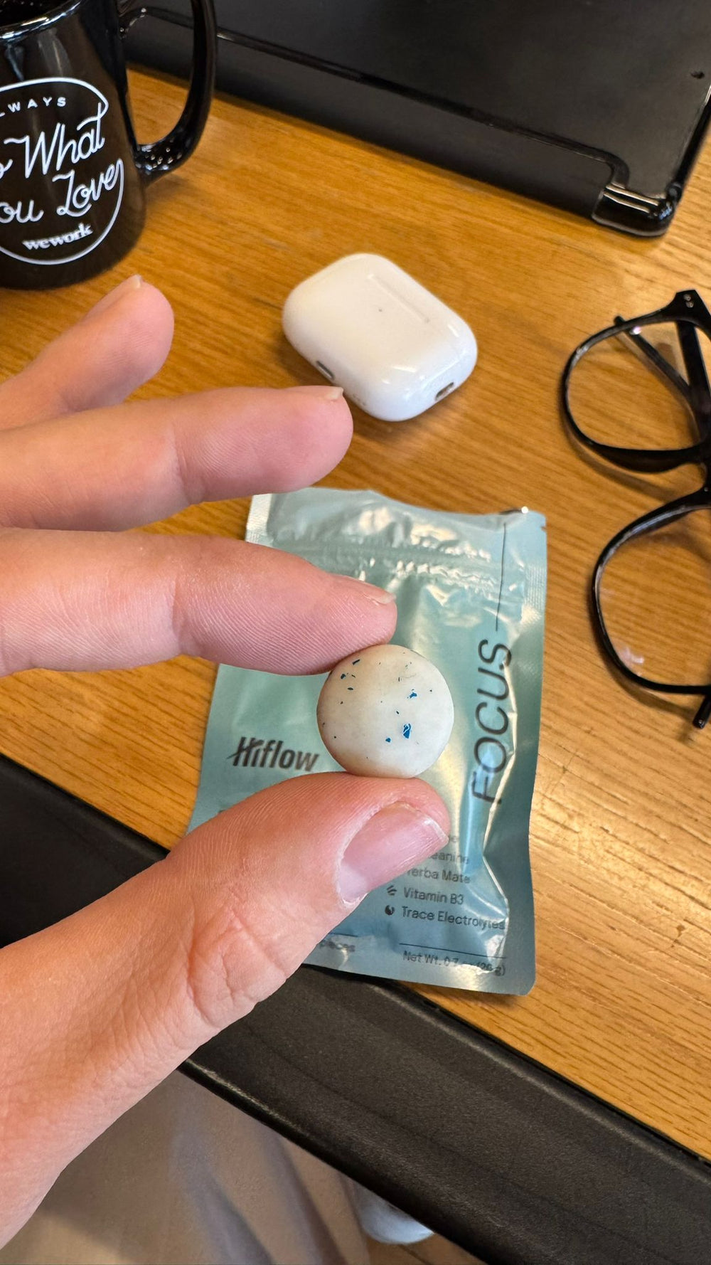 A person's hand holding a chewing gum piece with a Hiflow Focus gum pouch in the background laying on a desk.