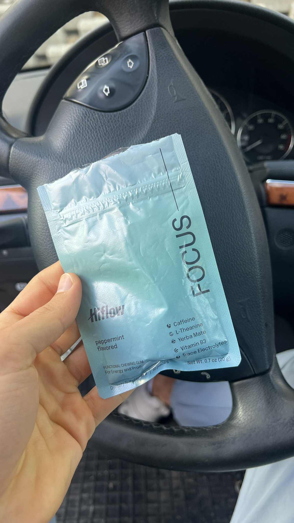 A hand holding a Hiflow Focus gum pouch inside a car.
